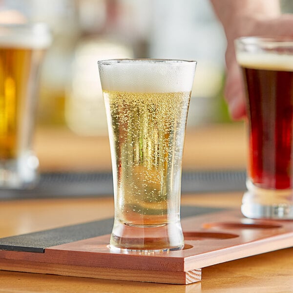 A person pouring beer into an Acopa flared Pilsner beer tasting glass on a table.