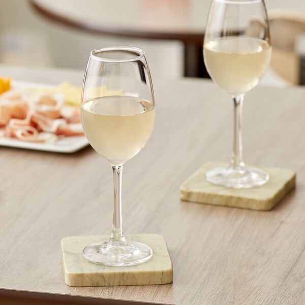 Two Acopa Select Blanc wine glasses filled with white wine on a table.