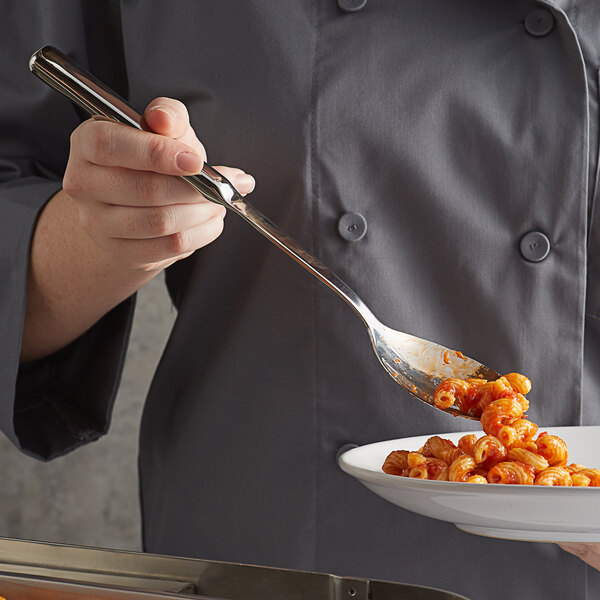 A person holding a Vollrath stainless steel notched serving spoon with food on it.