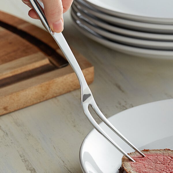 A hand holding a Vollrath stainless steel serving fork over a plate of steak.