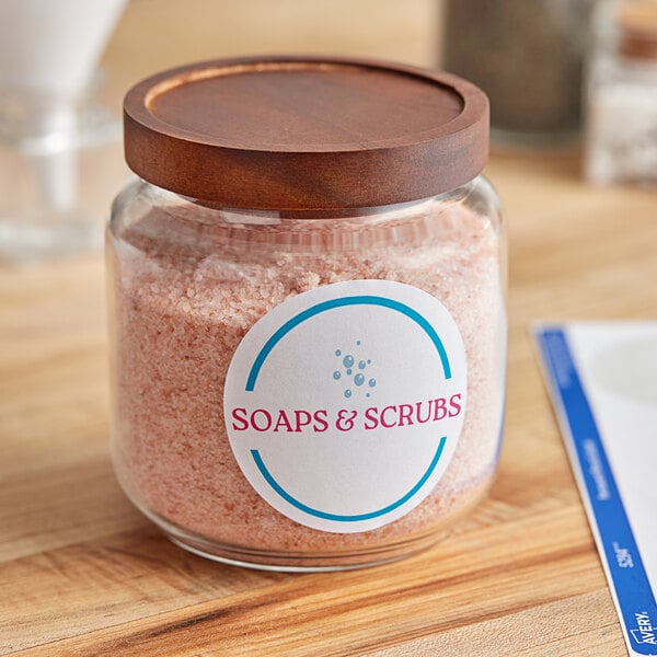 A jar of soaps and scrubs on a table with Avery High-Visibility Round White Labels.