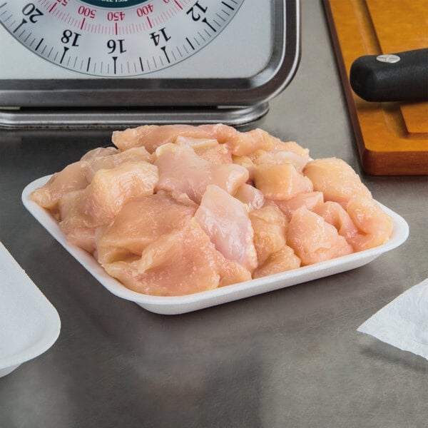 A white CKF foam meat tray on a counter filled with raw chicken meat.