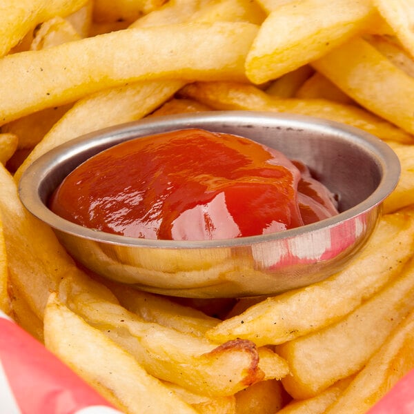 Stainless steel oval sauce cup filled with ketchup on french fries.