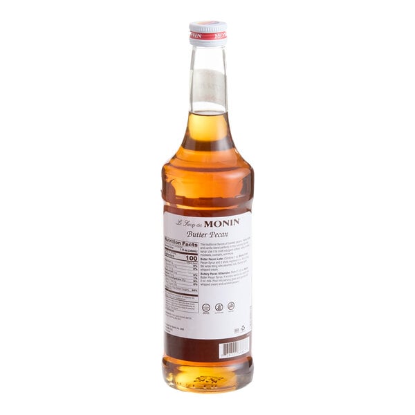 A clear glass bottle filled with amber-colored liquid, featuring a white label on the back that reads 'Monin Butter Pecan.'