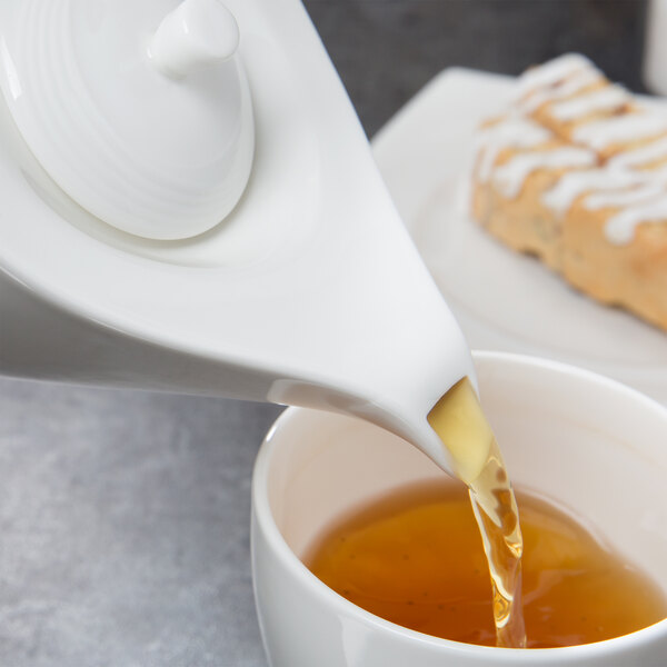 White porcelain Libbey tea being poured from a white teapot with a lid.