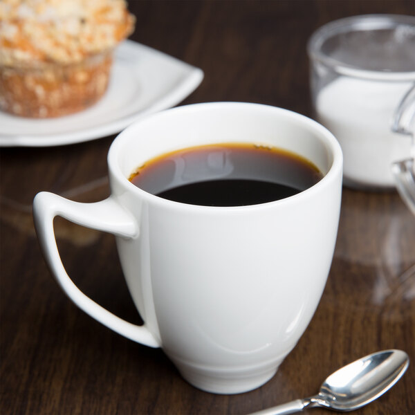 A white porcelain Royal Rideau mug filled with coffee on a table with a muffin.