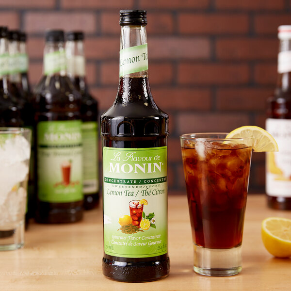 A Monin bottle of lemon tea concentrate next to a glass of iced tea.