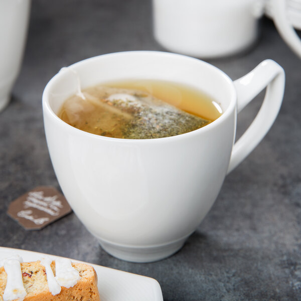 A Royal Rideau white porcelain cup filled with tea next to a cookie on a white saucer.