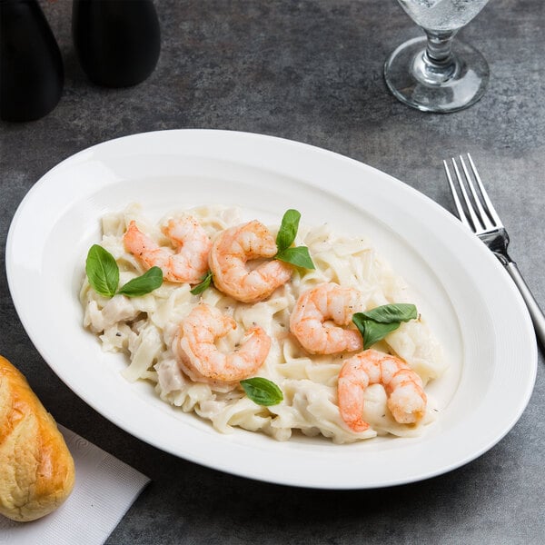 A white porcelain oval platter with shrimp pasta garnished with basil.