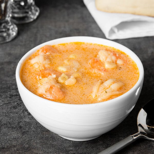 A white Reserve by Libbey Royal Rideau porcelain bowl filled with soup, shrimp, and cheese, with a spoon.