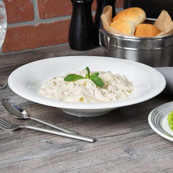 A bowl of pasta with a leafy green leaf on top next to silver utensils.