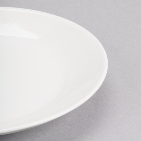 A close-up of a Reserve by Libbey white porcelain coupe plate with a white rim.