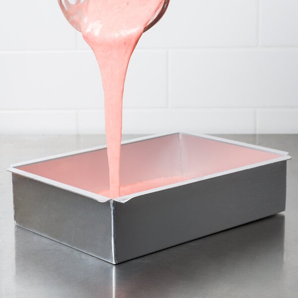 A person using an Ateco rectangular aluminum cake pan to pour pink liquid from a spoon.