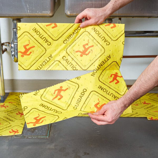A person holding a yellow Spilfyter absorbent pad with a yellow warning sign.