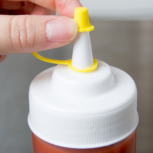 A hand holding a white Tablecraft squeeze bottle with a yellow cap.