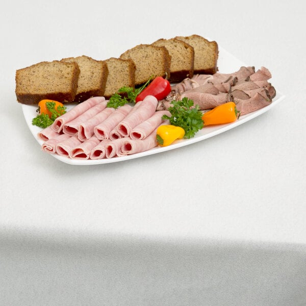 A plate of meat, bread, and vegetables on a table with a Hoffmaster white paper table cover.