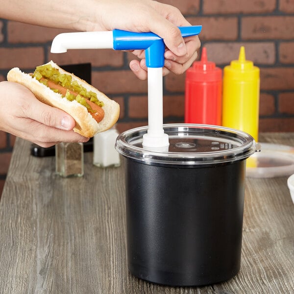 A person using a Cambro black condiment dispenser to add relish to a hot dog.