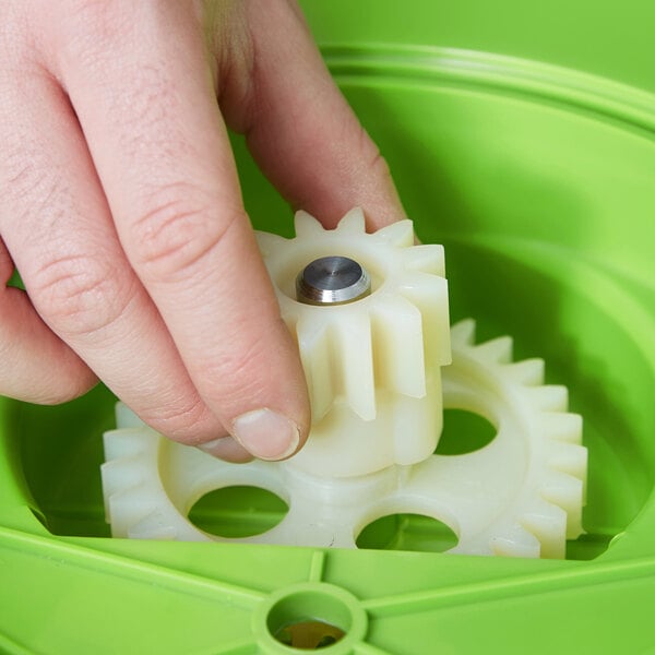A hand removes a white gear from a green Choice salad dryer.