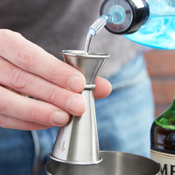 A person using an American Metalcraft stainless steel Japanese style jigger to pour a drink.