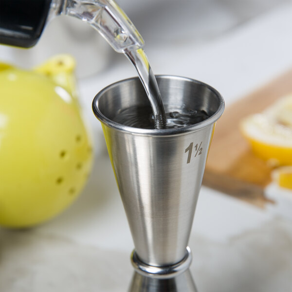 A person using an American Metalcraft stainless steel Japanese style jigger to pour liquid into a metal cup.