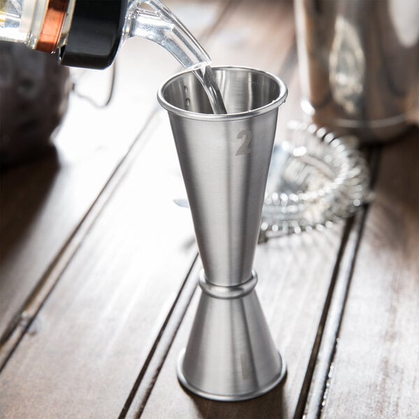 A person using an American Metalcraft stainless steel Japanese style jigger to pour a drink.