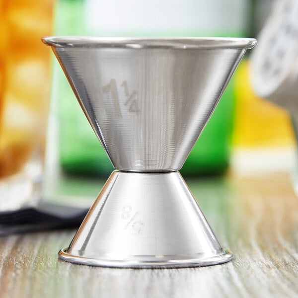 An American Metalcraft stainless steel jigger with measurements on a table.