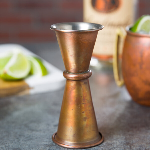 An American Metalcraft copper Japanese style jigger on a table with lime wedges.