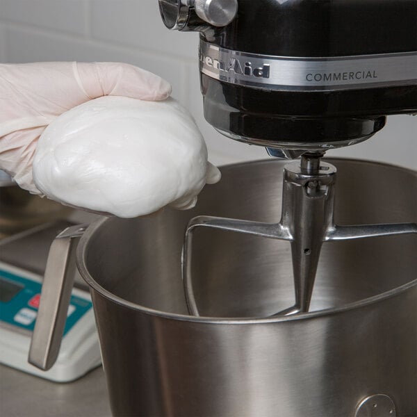 A person in gloves mixing Golden Barrel Creme Fondant in a bowl with a mixer.