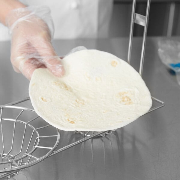 A hand using a Tablecraft tortilla fry basket to hold a tortilla.