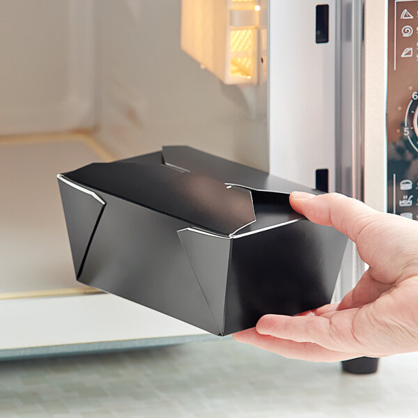 A hand holding a black Choice microwavable paper take-out box.