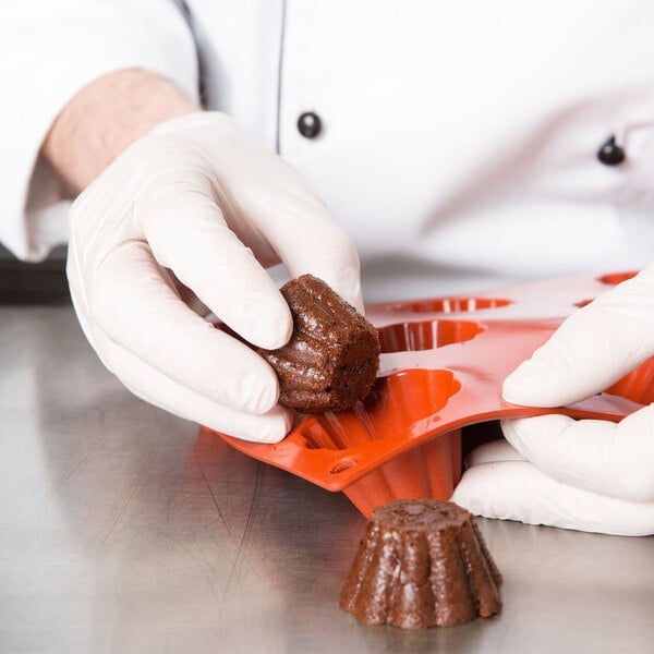 A person in gloves holding a small brown brioche made in a Matfer Bourgeat orange silicone mold.