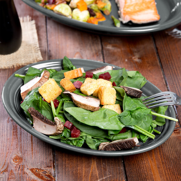 A Fiesta slate oval china platter with salad and a fork on a table.