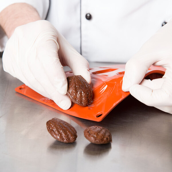 A gloved hand holding a brown Matfer Bourgeat madeleine.