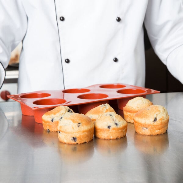 A chef in a white coat using a Matfer Bourgeat Gastroflex 6 compartment muffin mold to make muffins.