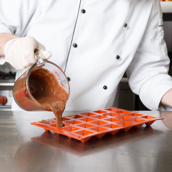 A chef pouring brown liquid into a Matfer Bourgeat mini pyramid mold.