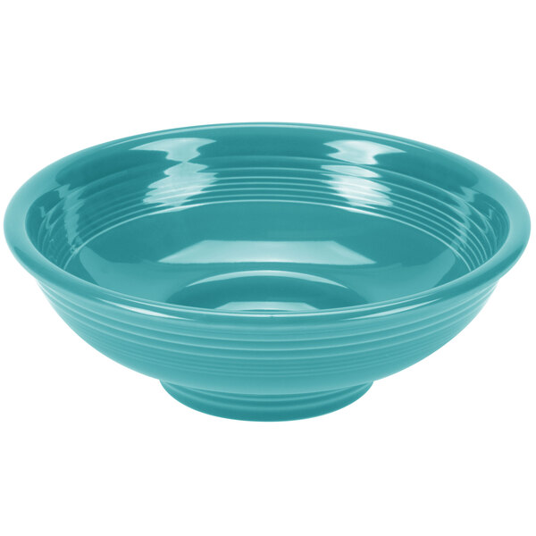 A turquoise Fiesta china pedestal serving bowl with ripples on a blue surface.