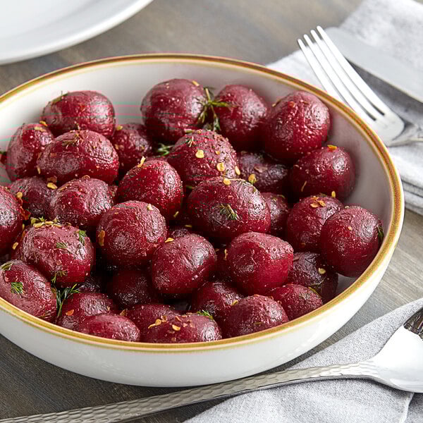 A bowl of Furmano's whole red beets on a table with a fork and knife.
