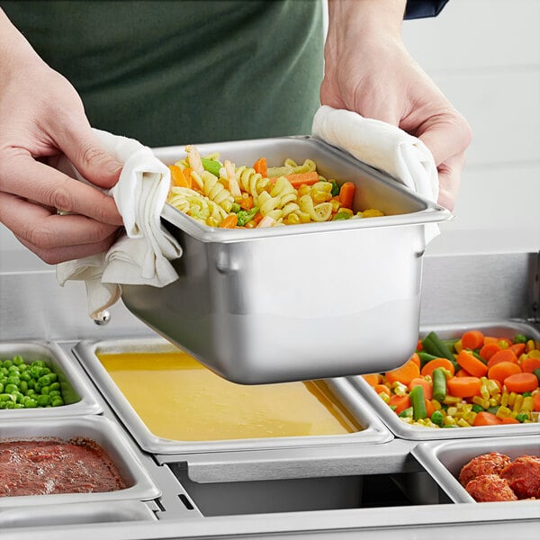 A person holding a dish with food in a Vigor stainless steel hotel pan.