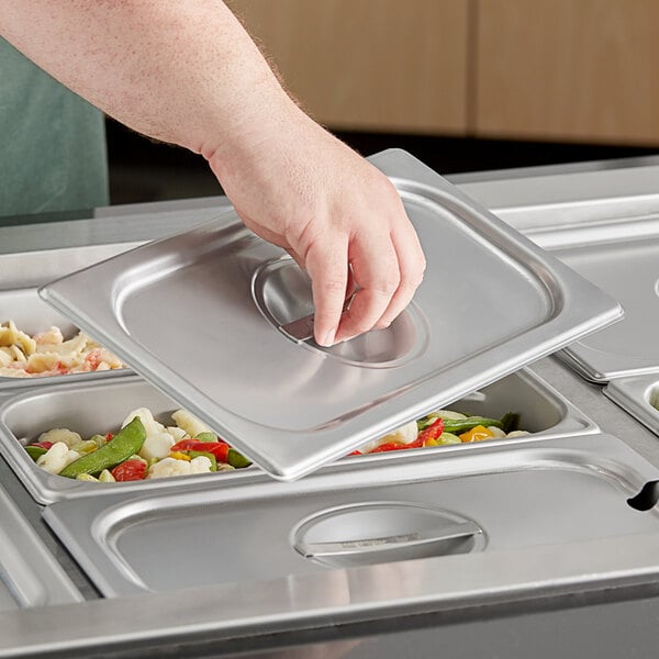 A hand holding a Vigor stainless steel tray with food in it.