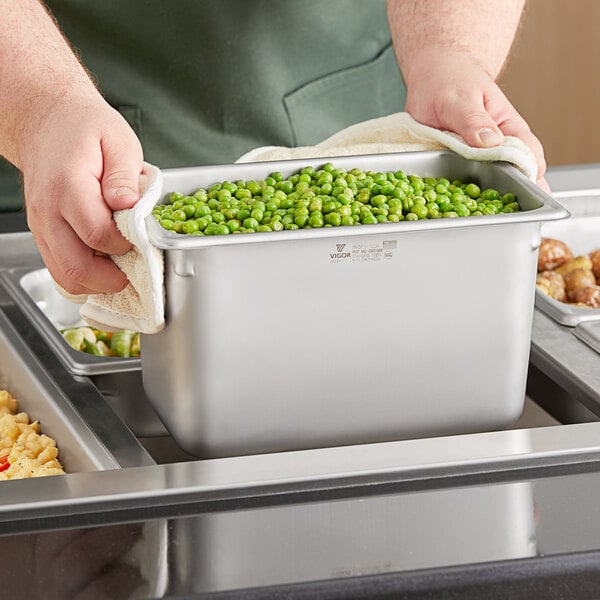 A person holding a Vigor 1/4 size stainless steel steam table pan filled with peas.