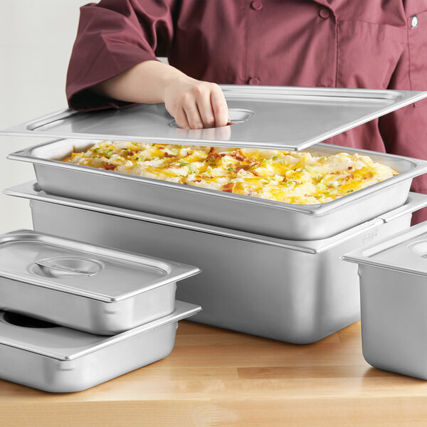 A woman using a Vigor stainless steel slotted steam table pan cover on a tray of food.