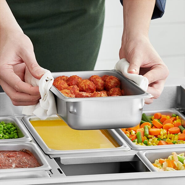 A person holding a Vigor stainless steel steam table pan full of meatballs.