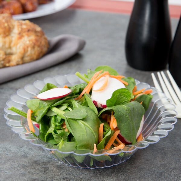 A vegetable salad in a Fineline clear plastic bowl with a fork and knife.