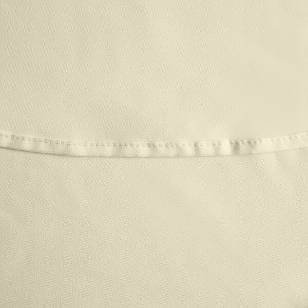 An ivory round 100% polyester table cover with a hemmed edge.