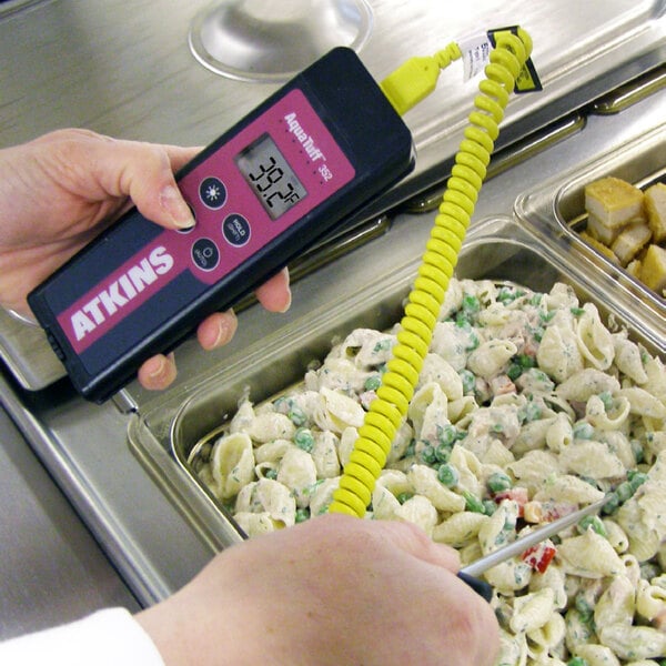 A person holding a Cooper-Atkins handheld thermometer to measure the temperature of food.
