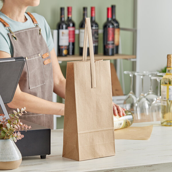 A person in an apron standing behind a counter with a brown paper bag with a handle holding two bottles of liquid.