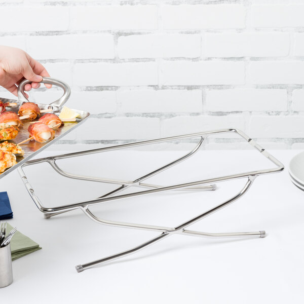 A hand holding an American Metalcraft stainless steel rectangular griddle stand with food on it.