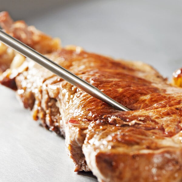 A DuraNeedle probe inserted into a piece of meat on a table.