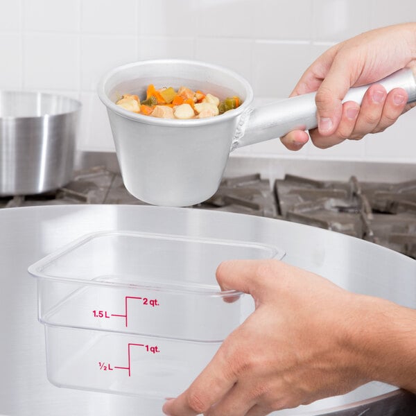 A hand using a Vollrath aluminum dipper to transfer food from a measuring cup to a container.