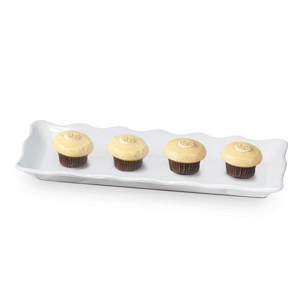 A white GET rectangular melamine tray with three cupcakes with white frosting on it.
